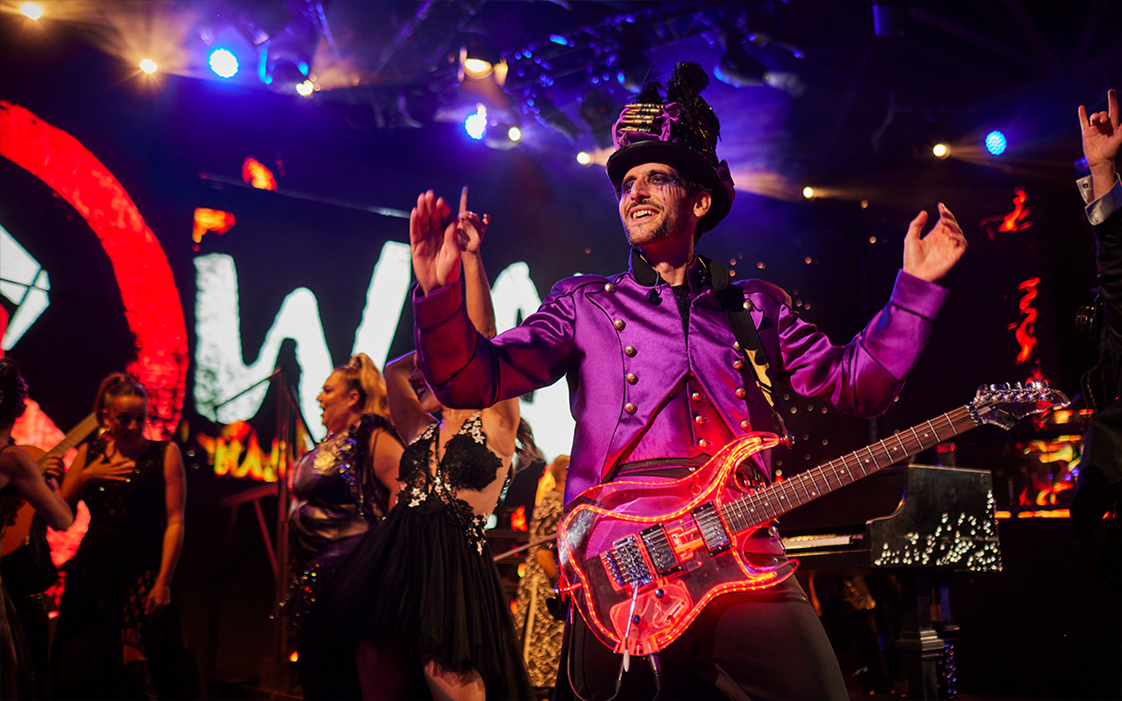 Performer in vibrant costume playing guitar on stage at WAH event.