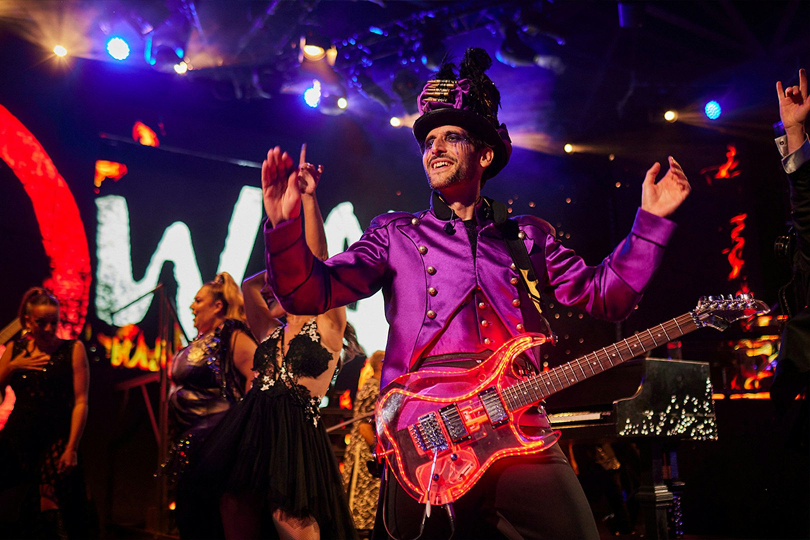 Performer in vibrant costume playing guitar on stage at WAH event.