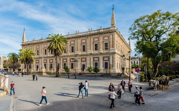 Seville's Archivo de Indias with tourists and horse-drawn carriage in the foreground.