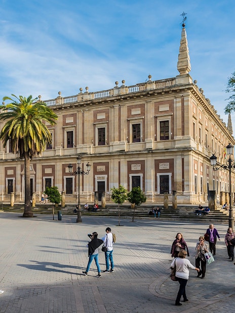 Seville's Archivo de Indias with tourists and horse-drawn carriage in the foreground.