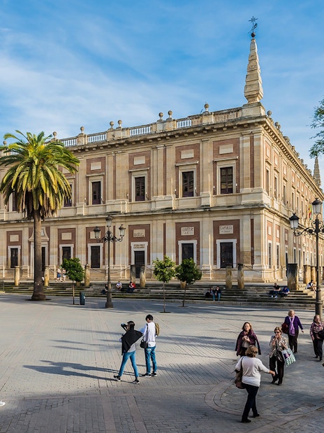 Seville's Archivo de Indias with tourists and horse-drawn carriage in the foreground.