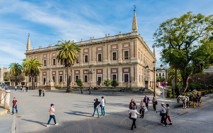 Seville's Archivo de Indias with tourists and horse-drawn carriage in the foreground.
