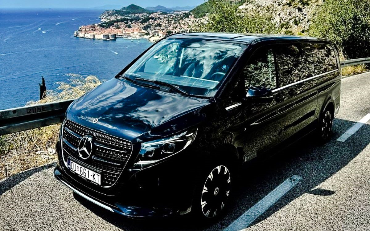 Luxury car on Adriatic coast road with view of Split in background.