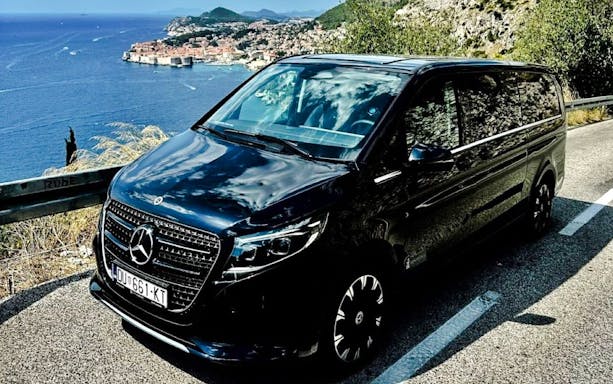 Luxury car on Adriatic coast road with view of Split in background.