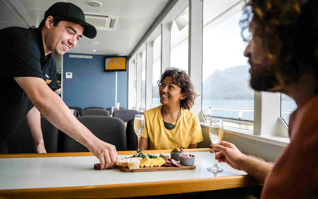 Two people enjoy champagne and a charcuterie board on the Doubtful Sound cruise.