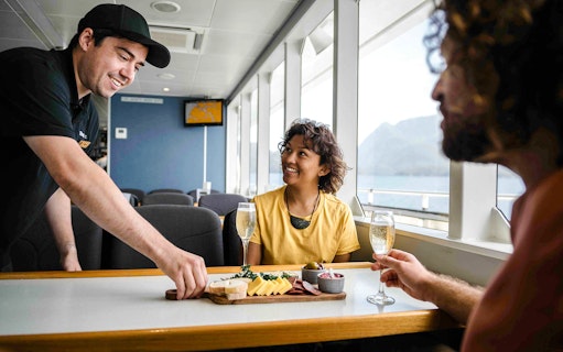 Two people enjoy champagne and a charcuterie board on the Doubtful Sound cruise.