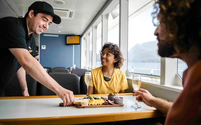 Two people enjoy champagne and a charcuterie board on the Doubtful Sound cruise.