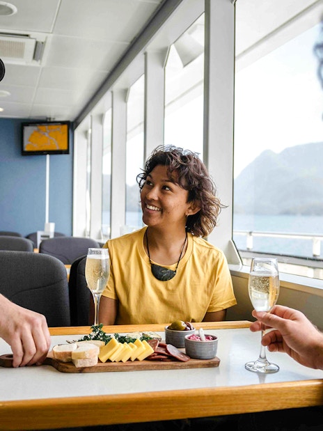 Two people enjoy champagne and a charcuterie board on the Doubtful Sound cruise.