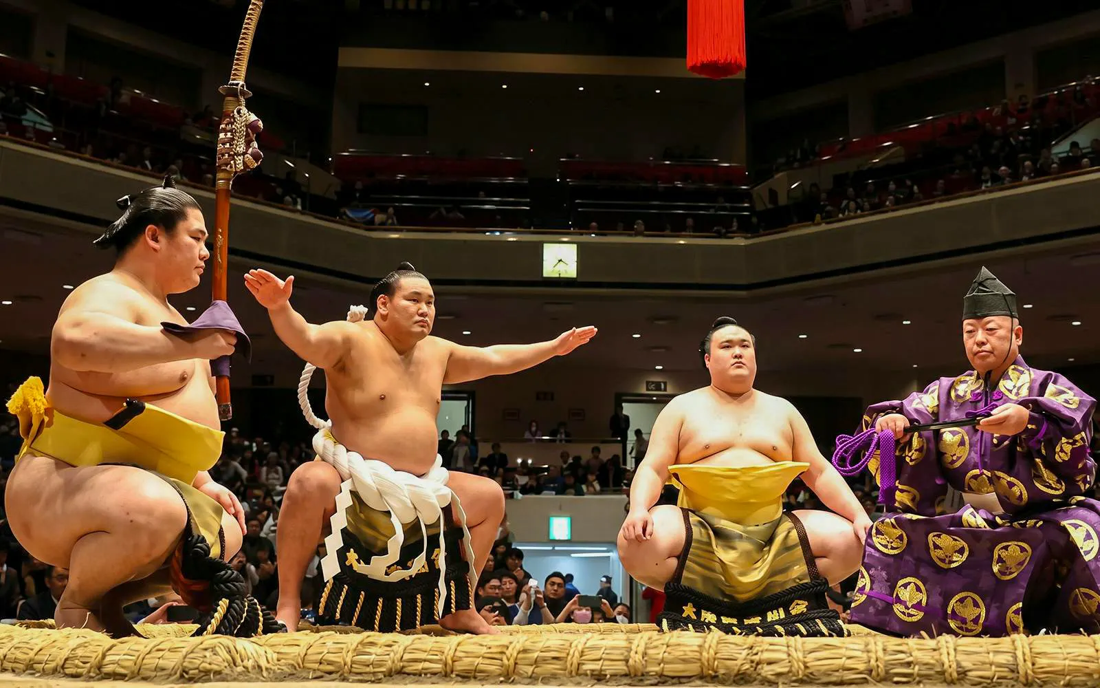 Sumo wrestlers and referee in traditional attire at Grand Sumo Tournament, Japan.