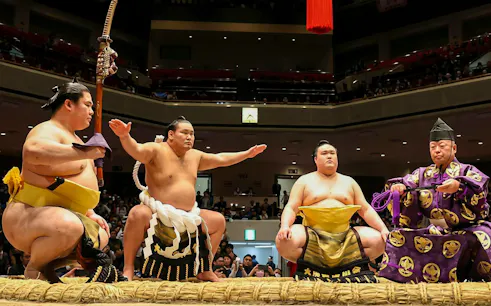Sumo wrestlers and referee in traditional attire at Grand Sumo Tournament, Japan.