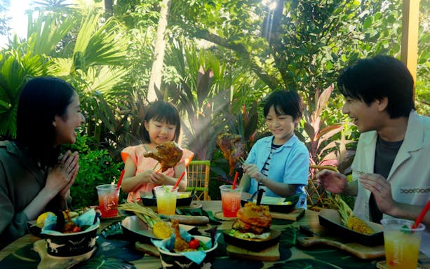 Family enjoying a meal at JUNGLIA OKINAWA Park surrounded by lush greenery.