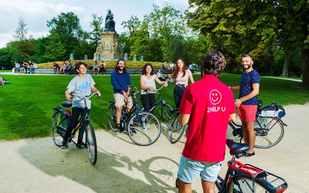 Cyclists riding along Amsterdam canal with historic buildings on guided bike tour.
