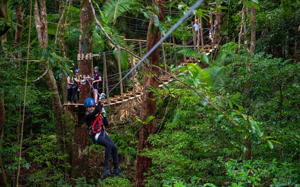Person ziplining through Daintree Rainforest with others waiting on a platform.