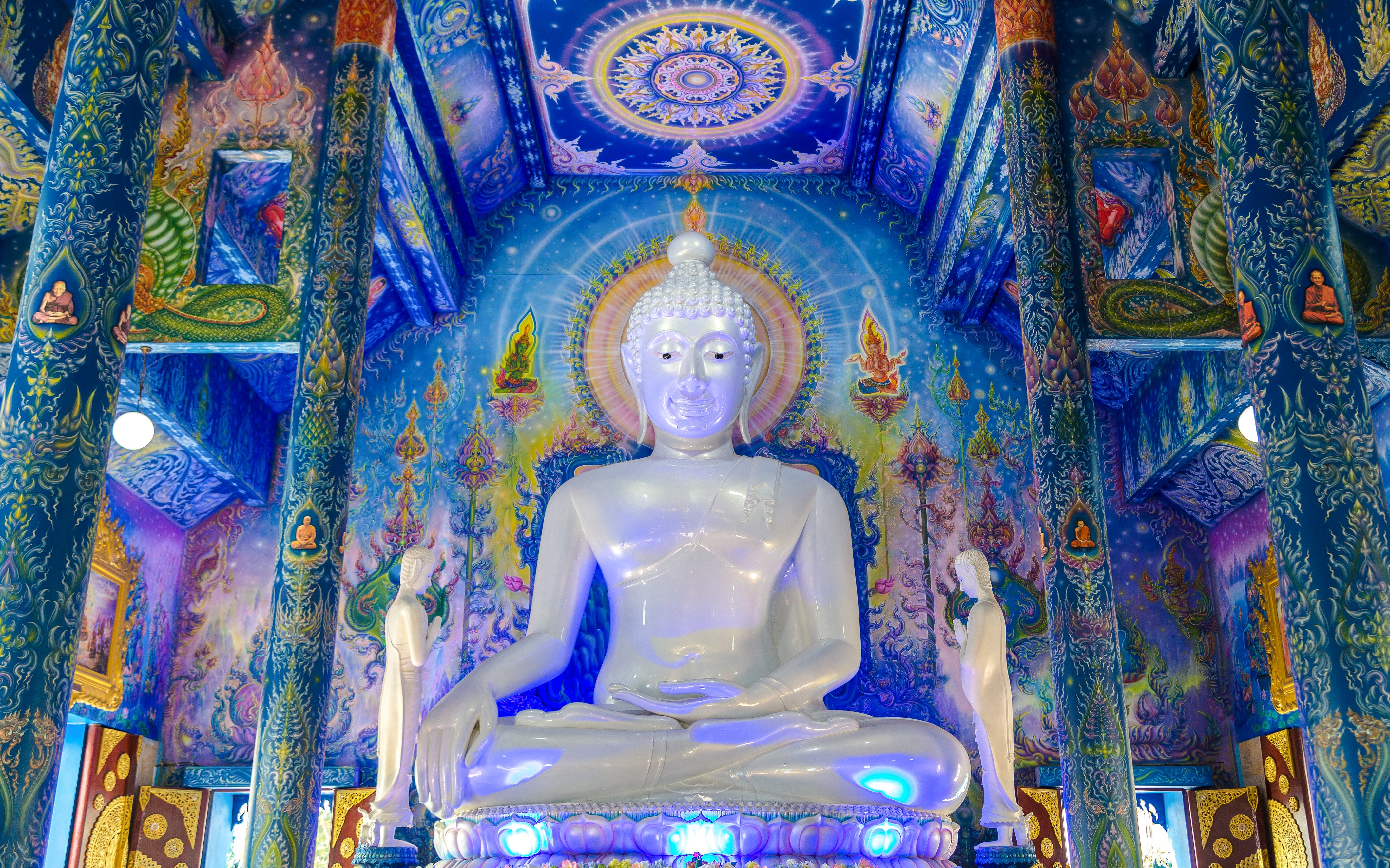 White Buddha statue inside Wat Rong Sua Ten, Chiang Rai, with vibrant blue murals.