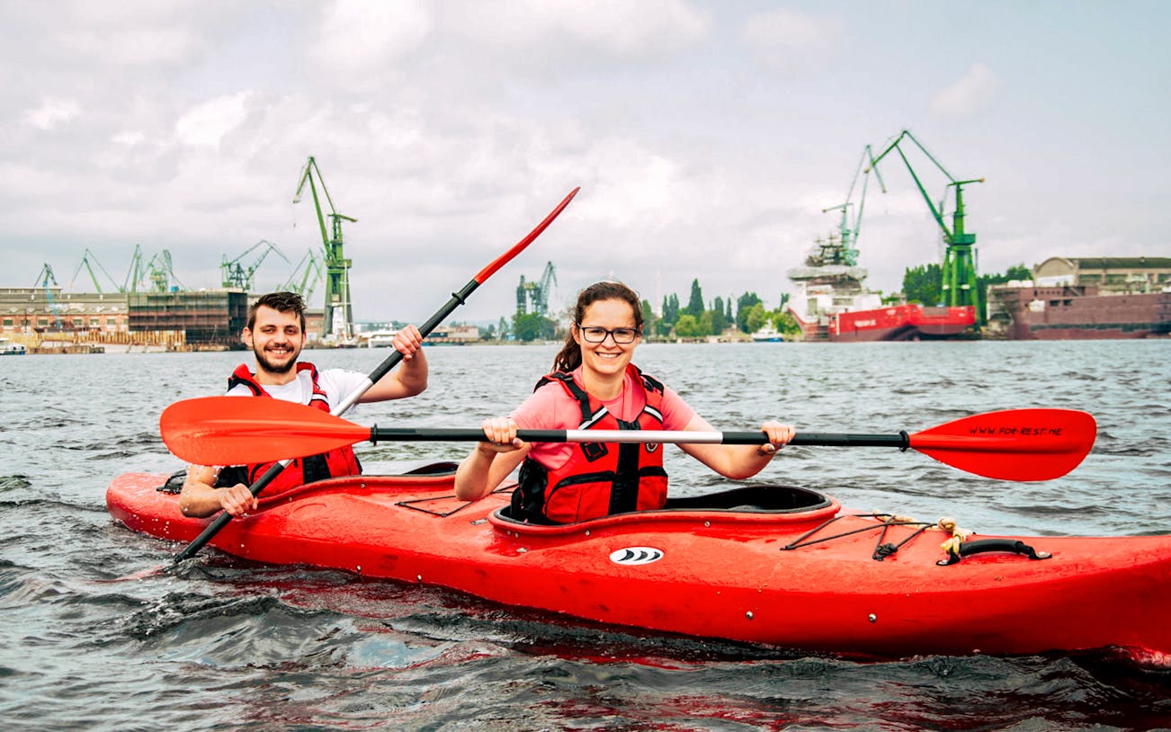 Kayakers paddling in Gdansk with shipyard cranes in the background.