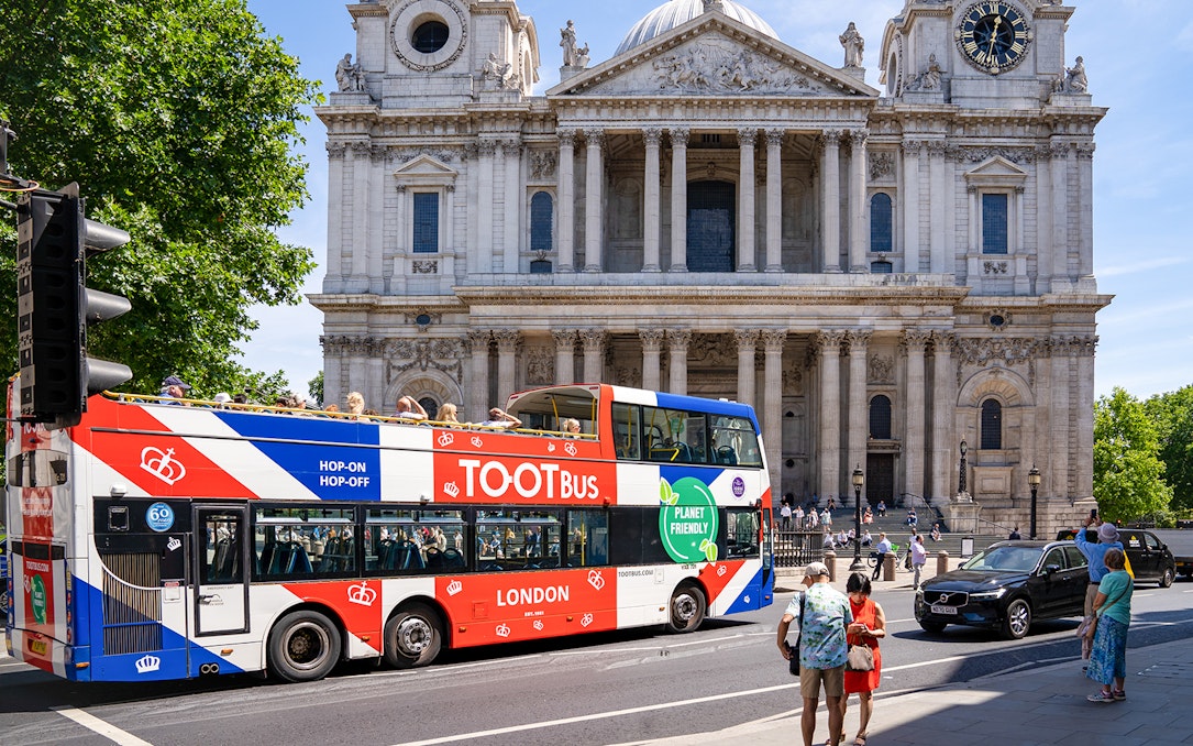 Tootbus passing St. Paul's Cathedral in London with passengers on a sunny day.