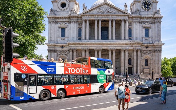 Tootbus passing St. Paul's Cathedral in London with passengers on a sunny day.