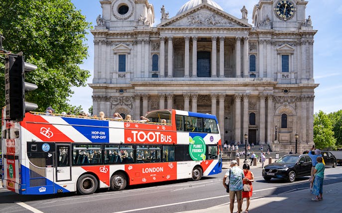 Tootbus passing St. Paul's Cathedral in London with passengers on a sunny day.