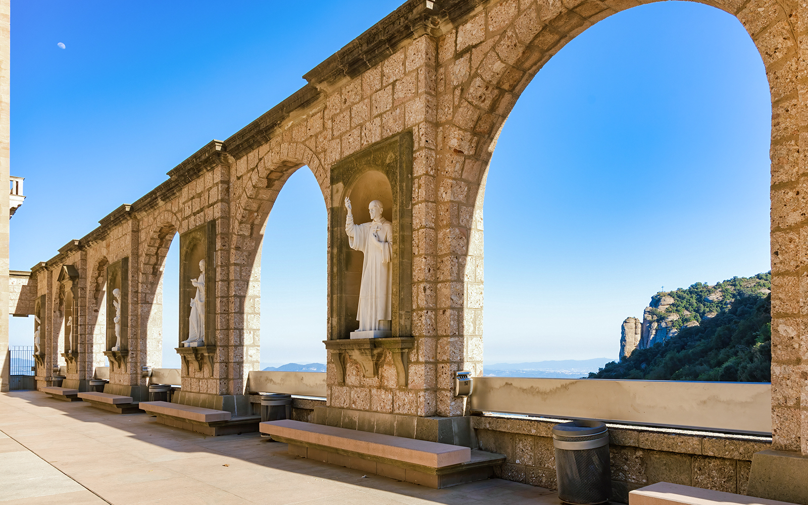 Stone arches and statues at Montserrat Monastery with mountain view, Spain.