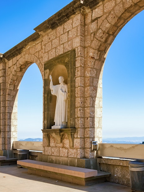 Stone arches and statues at Montserrat Monastery with mountain view, Spain.