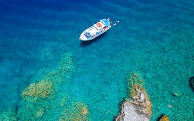Boat cruising near rocky coastline in Rhodes, Greece, with swimmers in clear blue water.