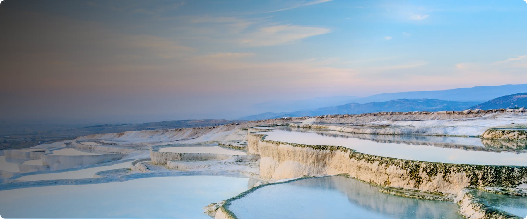Terraced thermal pools at Pamukkale, Turkey, with a scenic mountain backdrop.