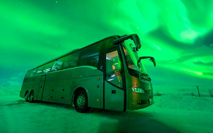 Bus under Northern Lights during chase tour in snowy landscape.