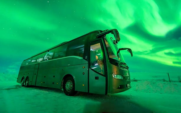 Bus under Northern Lights during chase tour in snowy landscape.