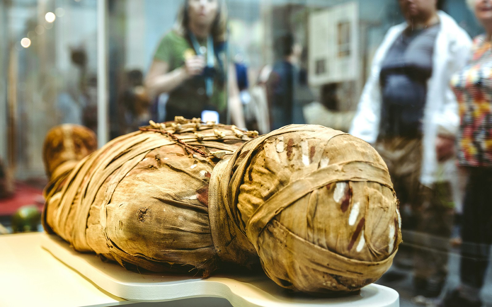 Ancient mummy display at the British Museum with visitors in the background.