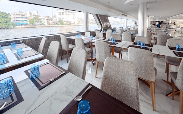 Dining area on The Luxury White Cruise ship with river view and elegant table settings.