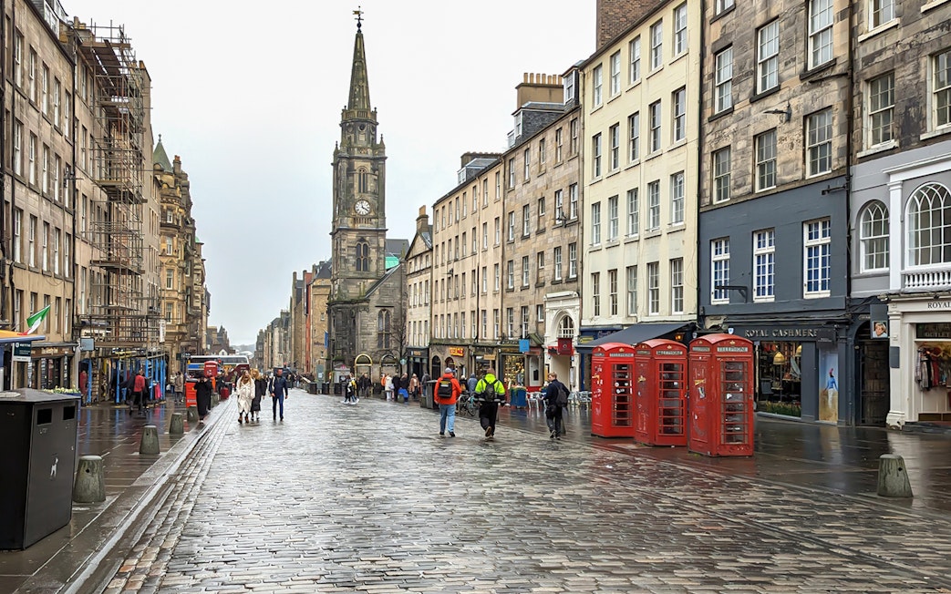 Cobblestone street on the Royal Mile, Edinburgh, with historic buildings and red phone booths.