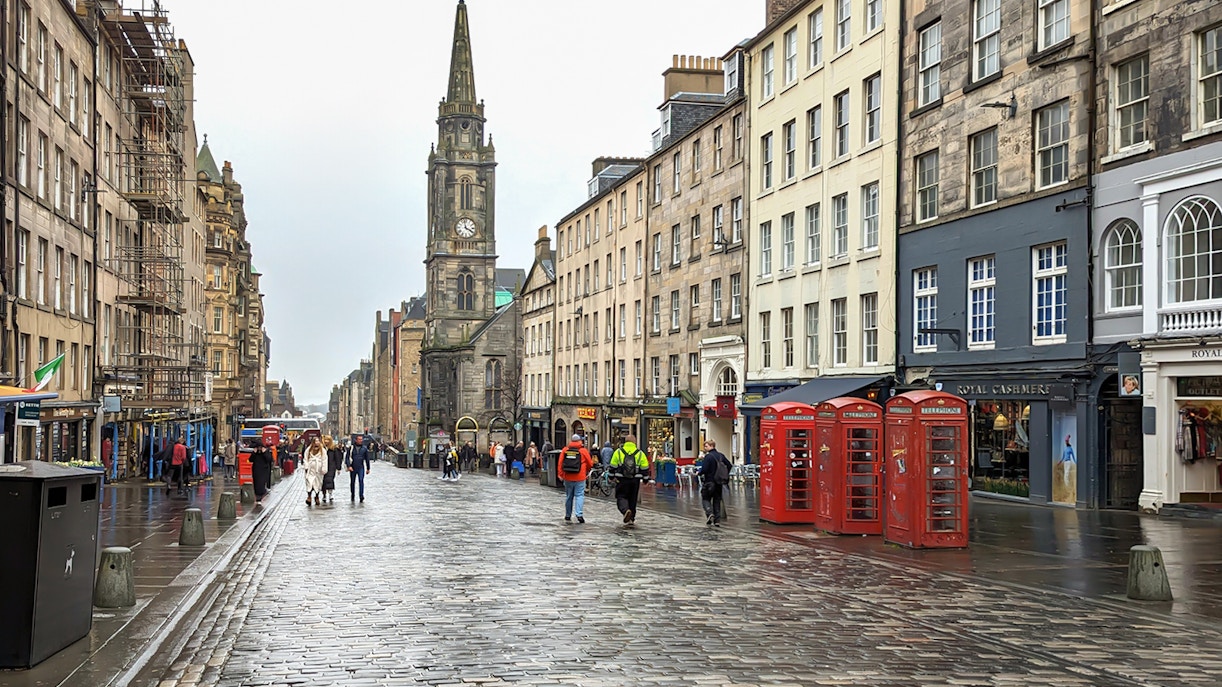 Cobblestone street on the Royal Mile, Edinburgh, with historic buildings and red phone booths.