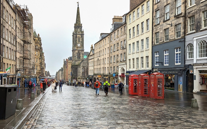 Cobblestone street on the Royal Mile, Edinburgh, with historic buildings and red phone booths.