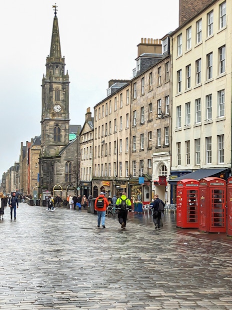 Cobblestone street on the Royal Mile, Edinburgh, with historic buildings and red phone booths.