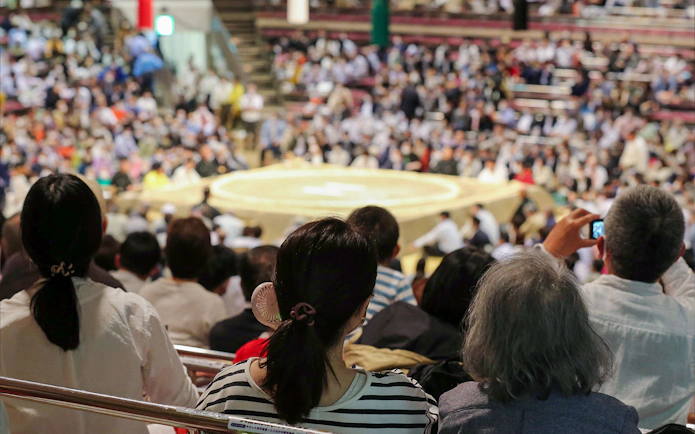 Spectators watching a sumo match in a crowded Tokyo arena.