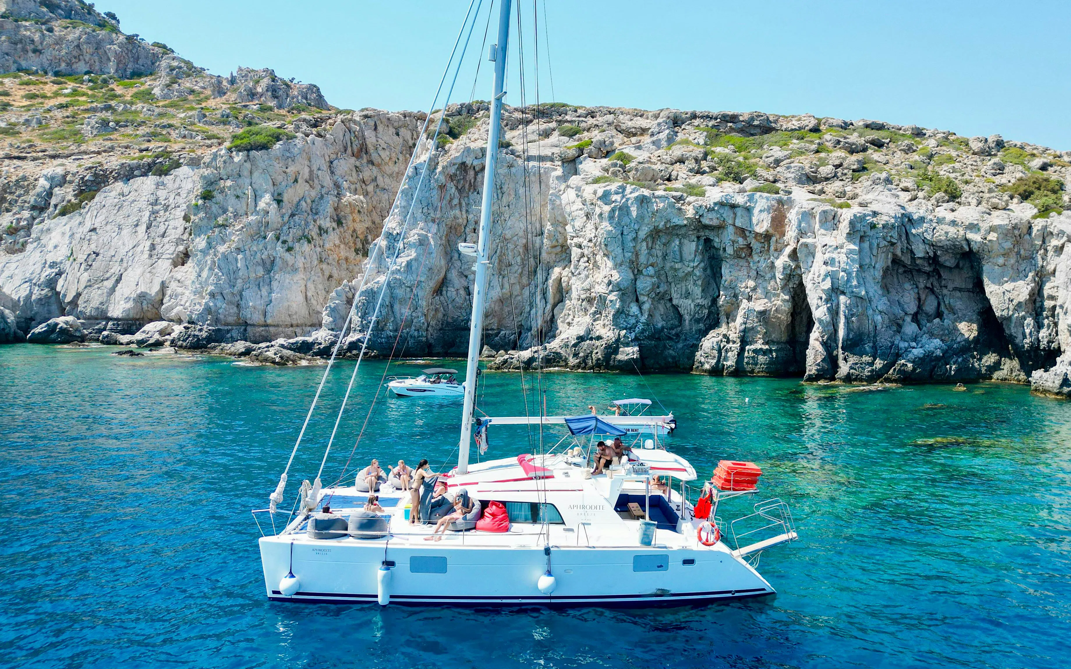 Catamaran with tourists cruising near rocky cliffs in Rhodes.