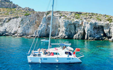 Catamaran with tourists cruising near rocky cliffs in Rhodes.