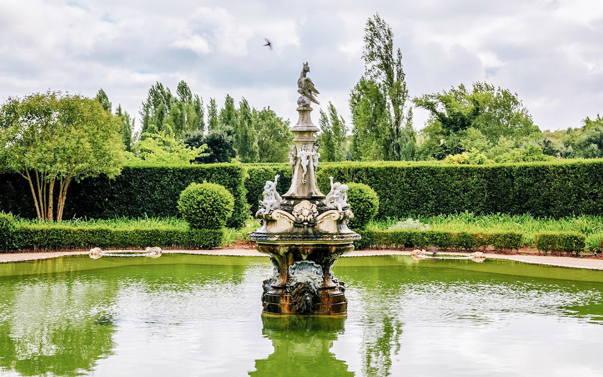 Fountain in Lake of Medals at National Palace of Queluz, surrounded by greenery.