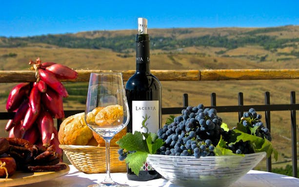 Wine bottle, glass, grapes, and bread on a table at a winery with vineyard view.