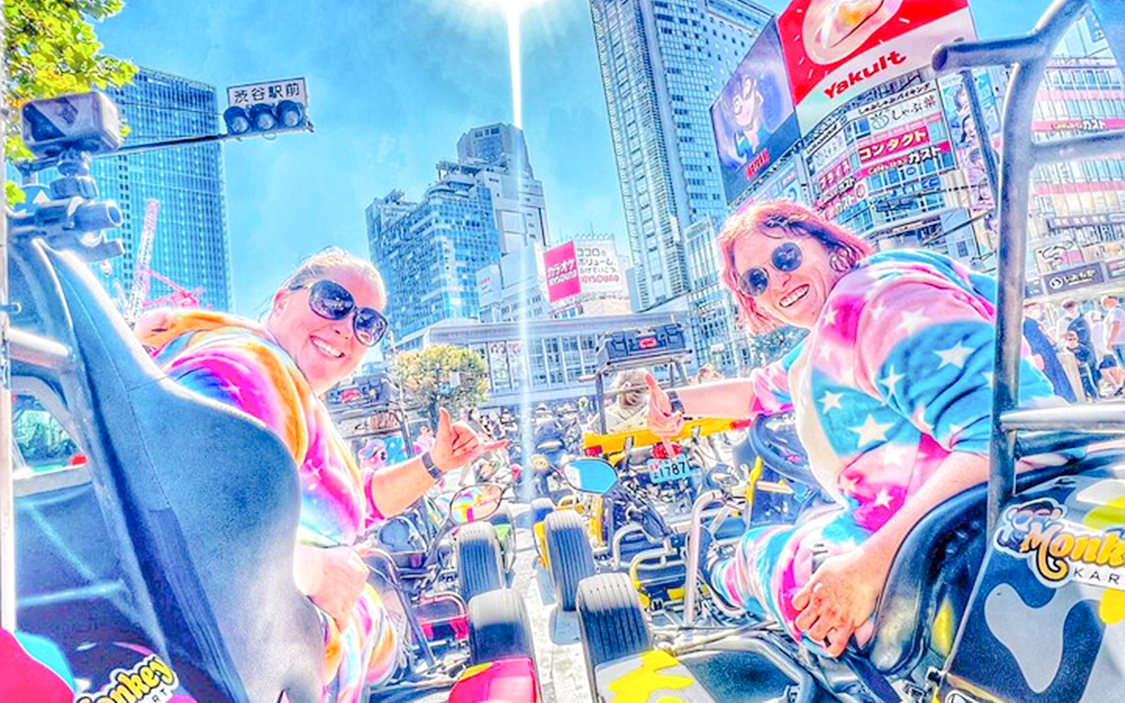 Two women in tie-dye costumes in go-karts at Shibuya Crossing, Tokyo.