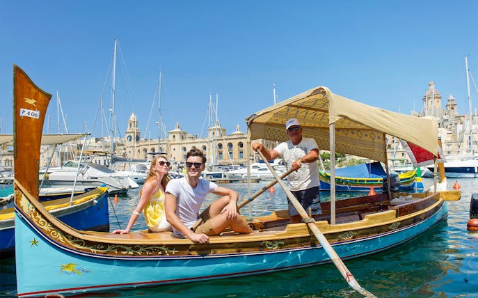 Boat tour with guide and tourists in the harbor of The Three Fortified Cities, Malta.