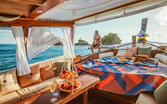 Longtail boat cruise in Krabi at sunset with people relaxing, fruits, and drinks.