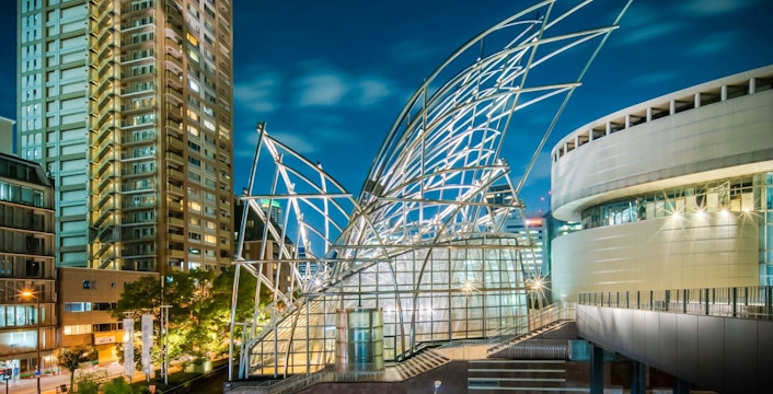 Steel architecture of The National Museum of Art, Osaka, illuminated at night with city skyline.
