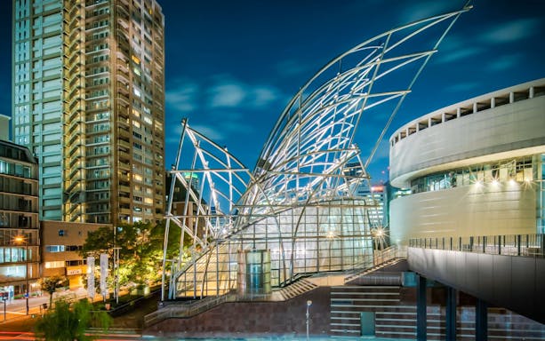 Steel architecture of The National Museum of Art, Osaka, illuminated at night with city skyline.