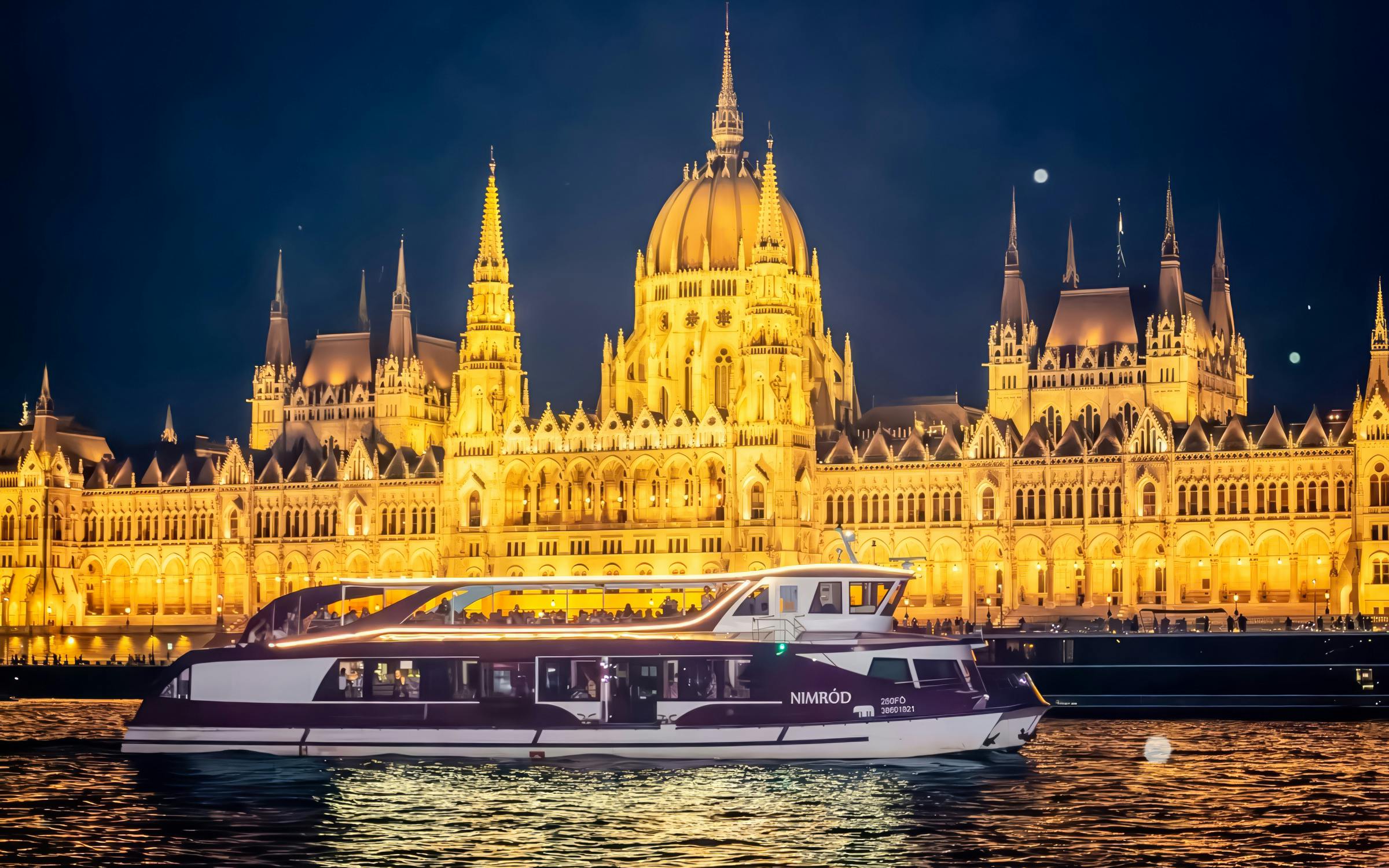 Cruise boat on Danube River with Budapest Parliament illuminated at night.