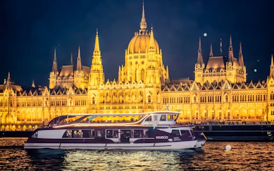 Cruise boat on Danube River with Budapest Parliament illuminated at night.