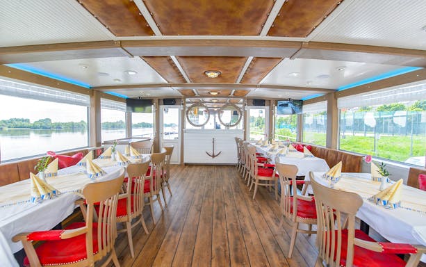 Interior of a Danube Canal cruise ship with dining tables set for a Viennese delicacies tour.
