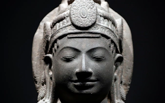 Stone sculpture of a serene face with intricate headdress at Asian Civilisations Museum.