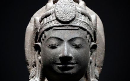 Stone sculpture of a serene face with intricate headdress at Asian Civilisations Museum.