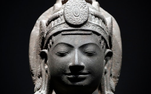 Stone sculpture of a serene face with intricate headdress at Asian Civilisations Museum.